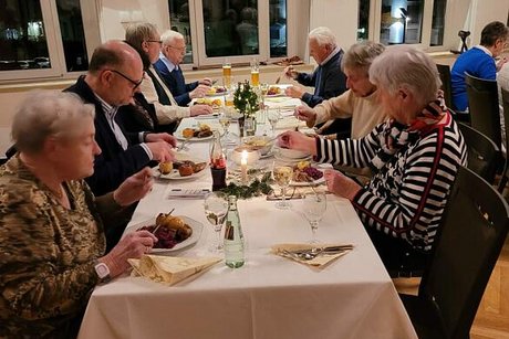 Menschen sitzen gemeinsam an einem langen Tisch beim Essen.