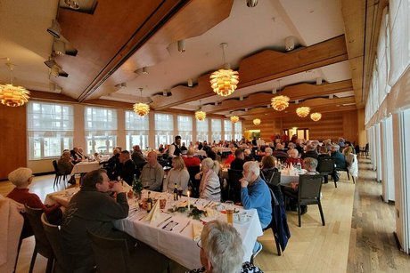 Menschen sitzen gemeinsam an langen Tischen in einem Saal.