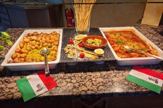 Italienisches Buffet: verschiedene Gerichte sind in großen weißen Schalen, geschmückt von Servietten mit Muster der italienischen Flagge auf einem großen Buffetangerichtet.