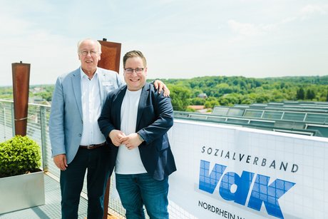 Zwei Männer stehen neben einem VdK-Banner , im Hintergrund die Umgebung der Zeche Zollverein.