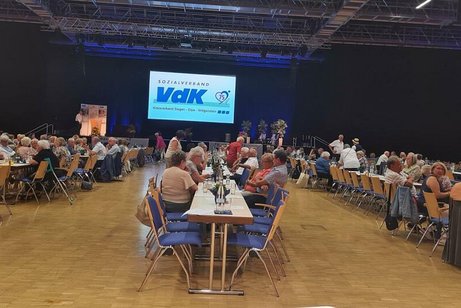 Viele Menschen sitzen an Tischen in einem Saal