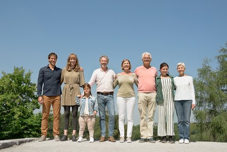 Menschen verschiedenen Alters mit und ohne Behinderung stehen untergehakt und l&auml;chelnd in einer Reihe in der Sonne