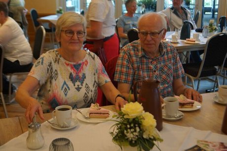 Eine Frau und ein Mann sitzen bei Kaffee und Kuchen an einem Tisch.