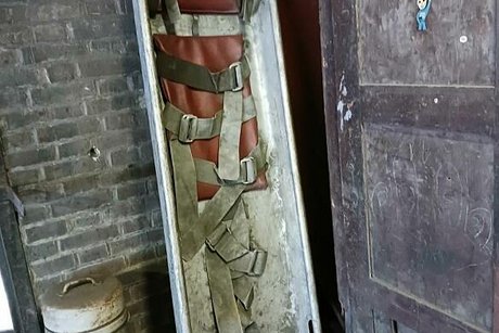 Eine alte Rettungstrage aus Stahl lehnt in der Ecke einer Werkhalle.