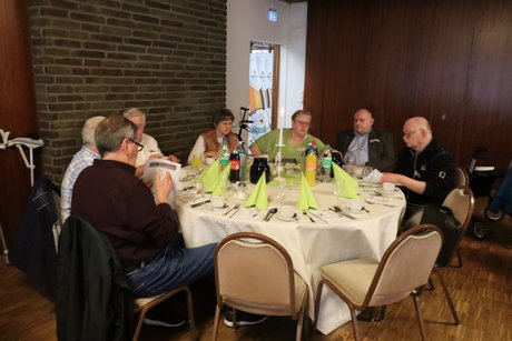 Sieben Personen sitzen an einem runden Tisch und unterhalten sich.