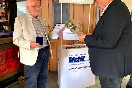 Jubilars- und Ehrenamts-Verleihung des VdK-Ortsverbandes Essen - Katernberg - Stoppenberg - Schonnebeck. Ein Mann spricht zu einem anderen Mann, der eine Silbermedaille und eine Urkunde in der Hand hält.