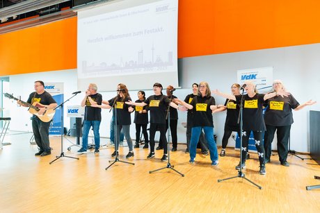 Ein Mann spielt auf einer Gitarre und singt dazu, während mehrere Personen mitsingen und tanzen.