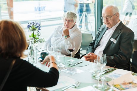 3 Personen sitzen an einem gedeckten Tisch und unterhalten sich.
