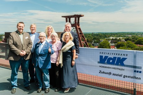 7 Personen stehen neben einem VdK-Banner und im Hintergrund der Förderturm der Zeche Zollverein.