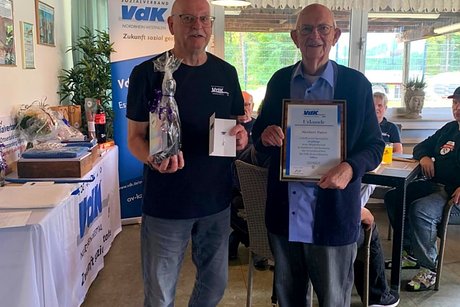 Jubilars- und Ehrenamts-Verleihung des VdK-Ortsverbandes Essen - Katernberg - Stoppenberg - Schonnebeck. Ein Mann übergibt eine Urkunde, eine Ehrennadel und ein Präsent an einen anderen Mann.
