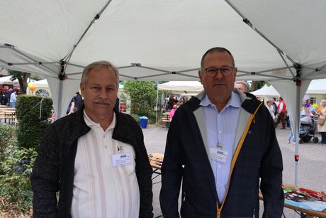 2 Männer stehen hinter einem Informationsstand.