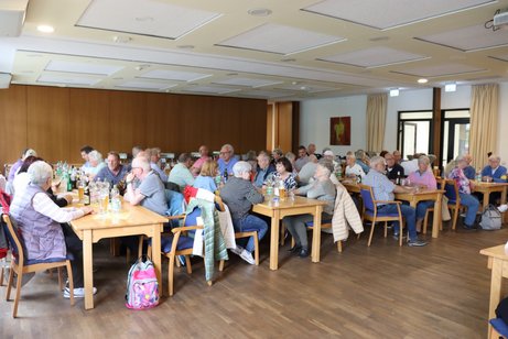 Mitglieder sitzen an drei langen Tischen und unterhalten sich.