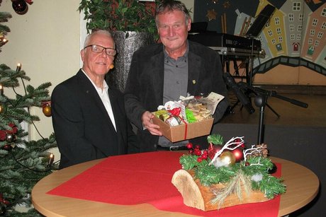 Zwei Männer stehen hinter einem weihnachtlich geschmückten Stehtisch. Einer der beiden hält einen Präsentkorb in der Hand.
