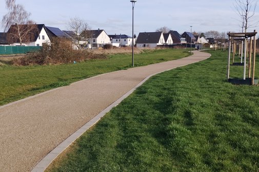 Das Foto zeigt einen gut befestigten Weg im Gr&uuml;nen in einem Baugebiet.