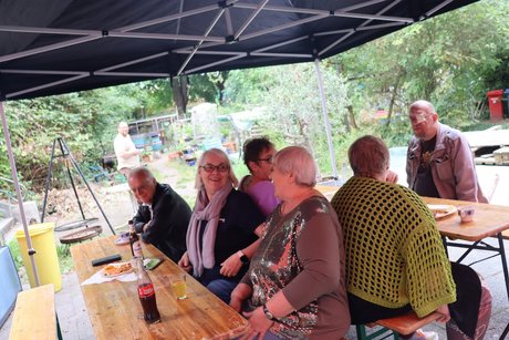 Mitglieder und Gäste im Außenbereich. Mehrere Menschen sitzen im Außenbereich und unterhalten sich.