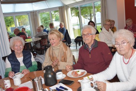Mitglieder sitzen am Tisch und trinken Kaffee und essen Kuchen. Dabei hören sie aufmerksam zu. Auch der Ehrenvorsitzende Manfred Radermacher sitzt am Tisch.