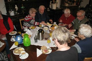 Sechs Menschen sitzen gemeinsam beim Frühstück an einem Tisch.