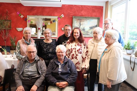 Mehrere Personen stehen oder sitzen f&uuml;r ein Gruppenbild zusammen.