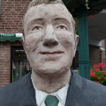 Die Skulptur Alltagsmensch in Straelen ist ein Mann mit blondem Haar, grauer Jacke, weißem Hemd und grüner Krawatte.