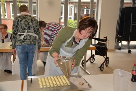 Eine junge Frau füllt mit einem Edelstahltrichter Ganache in Hohlraumkugeln aus weißer Schokolade.