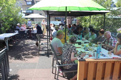 Menschen sitzen an mehreren Tischen im Au&szlig;enbereich,