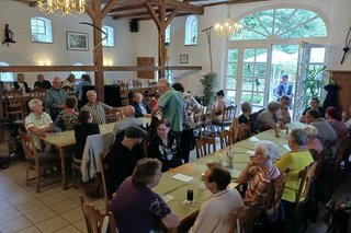 Menschen sitzen in einer Gaststube an langen Tischen.