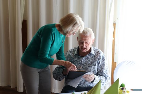 Jahreshauptversammlung 2026 Eine Frau steht neben einem sitzenden Mann und läßt ihn auf der Teilnehmerliste unterschreiben.