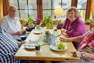 Zwei Männer und zwei Frauen sitzen gemeinsam an einem Tisch vor einem Fenster.