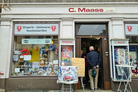 Außenfassade des historischen Drogerie- und Spielwarenladens mit der Aufschrift C. Maass über der Tür, durch die gerade ein Herr den Laden betritt.