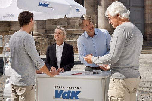 Menschen am VdK-Infostand Eine Mitarbeiterin und ein Mitarbeiter an einem VdK-Infostand informieren gerade zwei interessierte Passanten.