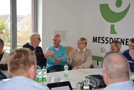 Menschen sitzen gemeinsam um einen großen Tisch herum und reden.