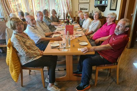Menschen sitzen gemeinsam an einem gedeckten Holztisch.