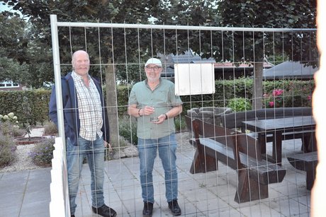 Zwei Männer stehen hinter einem Zaun und schauen belustigt in die Kamera