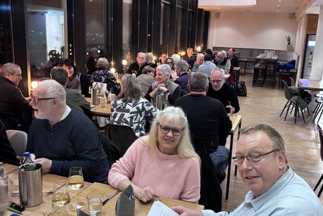 Das Foto wurde in den Saal hinein fotografiert. Es sind die Teilnehmenden an Tischen sitzend zu sehen.