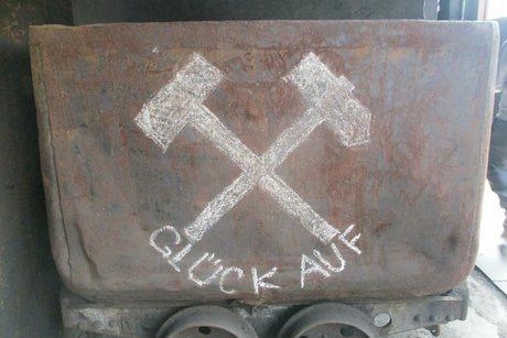 Auf einer alten rostigen Lore sind in weißer Kreidefarbe zwei gekreuzte Hammer aufgemalt und der Spruch Glück auf