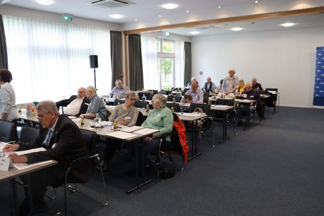 Mehrere Personen sitzen an langen Tischen.