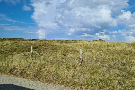 Dünenlandschaft bis zum Horizont, darüber ziehen am blauen Himmel einige Quellwolken.