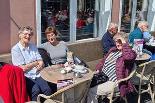 Drei Frauen sitzen um einen Bistro-Tisch herum und genießen die Sonne.