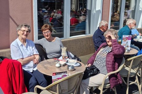 Drei Frauen sitzen um einen Bistro-Tisch herum und genießen die Sonne.