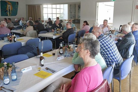 Viele Menschen sitzen in einem Saal an langen Tischen.