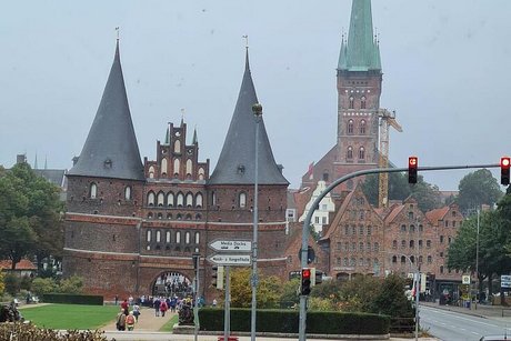 Foto einer beampelten Kreuzung mit Blumenrabatten, Holstentor und St. Petri Kirche im Hintergrund