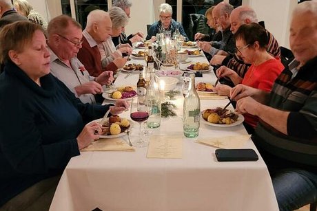 Menschen sitzen gemeinsam an einem langen Tisch beim Essen.