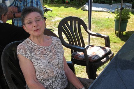 Grillnachmittag. Eine Frau blickt in die Kamera, dahinter sind noch 2 weitere Personen zu erkennen.