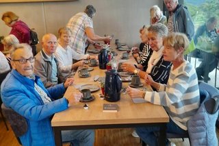 Menschen sitzen gemeinsam beim Essen an einem langen Holztisch.