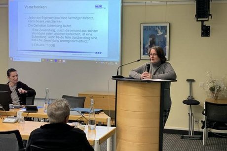 Das Bild zeigt im H&ouml;rsaal am Rednerpult Frau die RA'in und Kreisvverbandsvorsitzende Katharina Batz mit aufmersamen Zuh&ouml;rer/innen