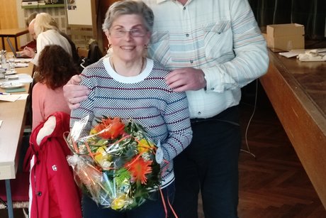 Vorsitzender steht hinter Kassenpr&uuml;ferin, die einen Blumenstrau&szlig; h&auml;lt