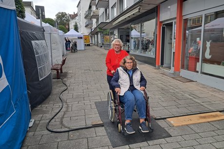 Eine Frau hilft einer Frau, die im Rollstuhl sitzt, über die Hindernisse