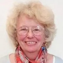 Abgebildet ist Christel Braun. Sie lächelt in die Kamera, trägt ein geblümtes Tuch, hat graublonde Haare und ist Brillenträgerin.
