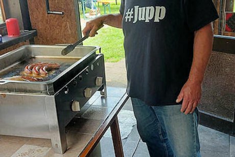 Ein Mann steht mit einer Grillzange an einem Indoor-Tischgrill und schunzelt in die Kamera.