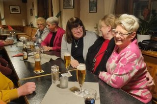 Fünf Frauen sitzen bei Getränken entlang einer langen Tafel und reden und lachen.